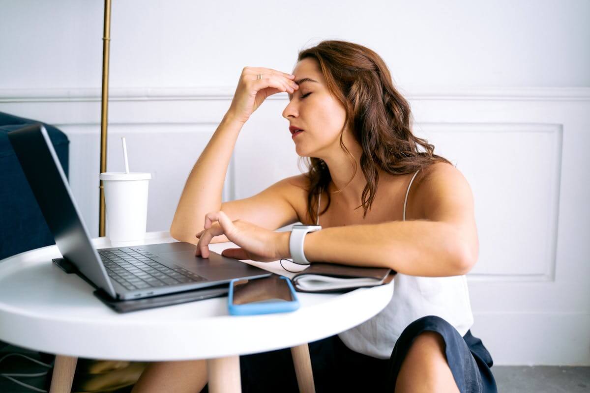 Stressed woman on her laptop with her fingertips on her forehead in frustration